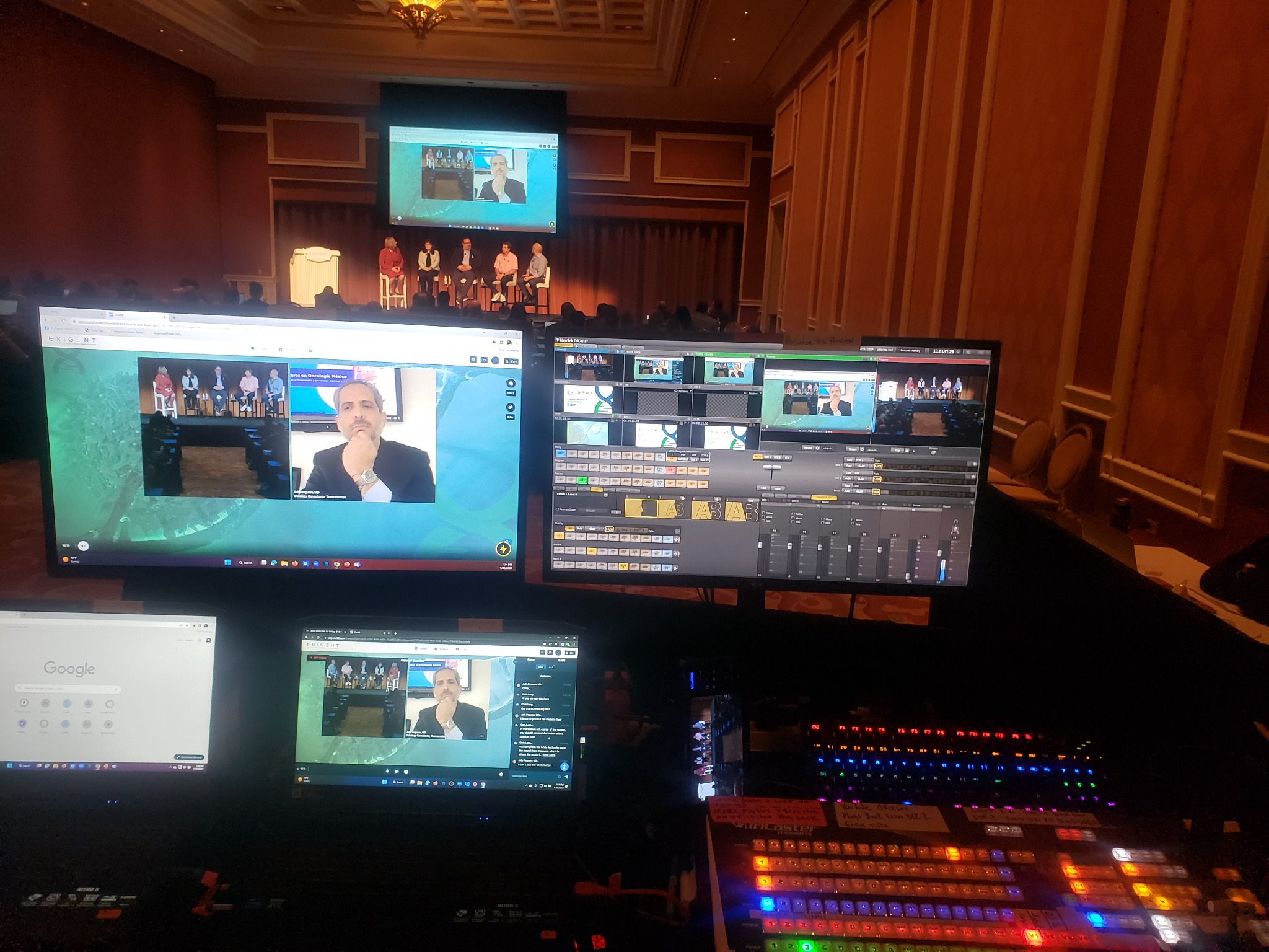 Ballroom panel discussion with a remote guest on the stage screen and live streaming monitors and controls in the foreground