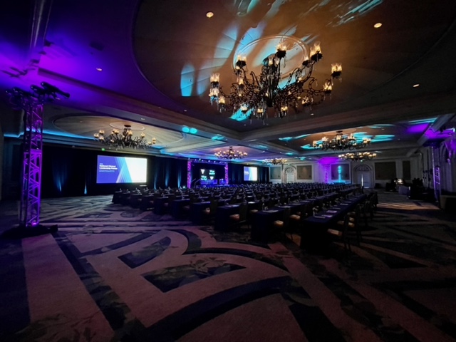 Conference ballroom with stage screens, seating and purple and blue event lighting
