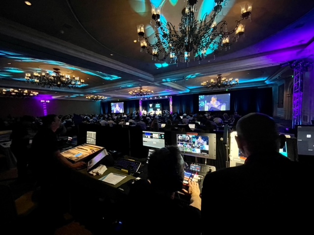 Production crew and monitors overlooking a live conference audience and stage
